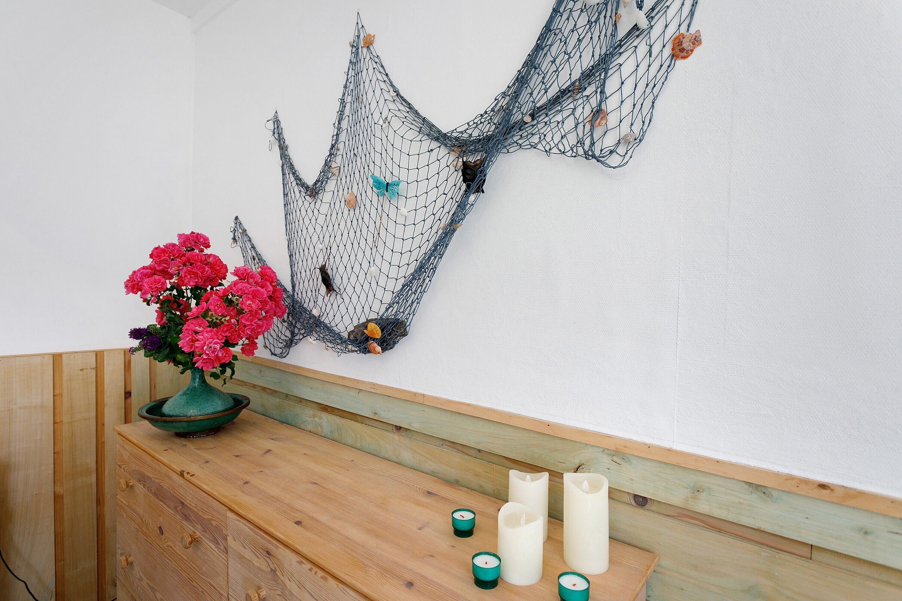 Un banc en bois agrémenté d’un vase de fleurs, de bougies et d’un filet décoratif fixé au mur.
