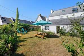 Ein Garten mit Picknicktisch und Stühlen, umgeben von Grünpflanzen und einem Haus.