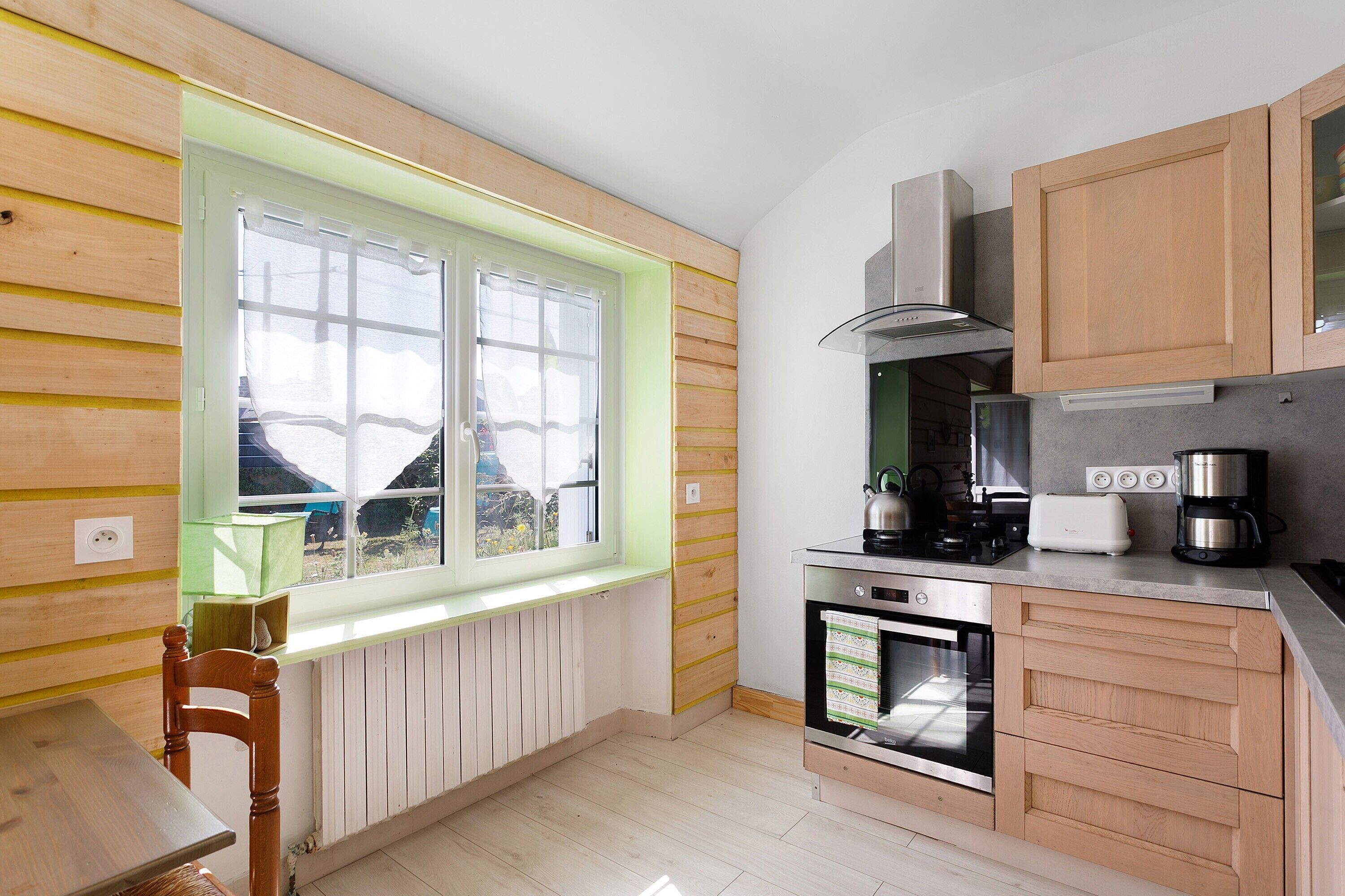 Une cuisine avec des meubles de rangement en bois, une fenêtre, une cuisinière et un évier.