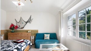 A bedroom with a bed, a sofa, a coffee table, a dresser, and a window with a view of greenery. - Holiday Home “Le Sémaphore” – Just 50m from the Beach (Plougasnou)