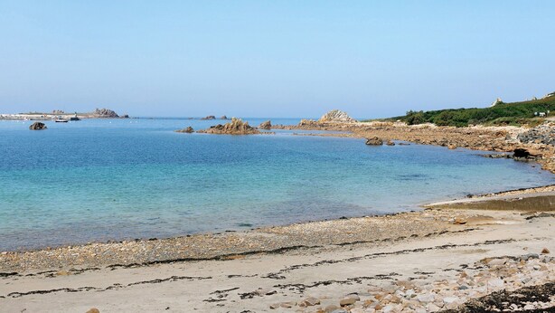 A coastal landscape with clear water, rocky shore, and distant buildings. - Holiday Home “Le Sémaphore” – Just 50m from the Beach (Plougasnou)