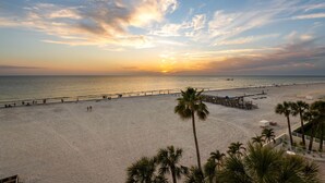 Ein Strand mit einer Holzstege, Palmen und einem Sonnenuntergang.