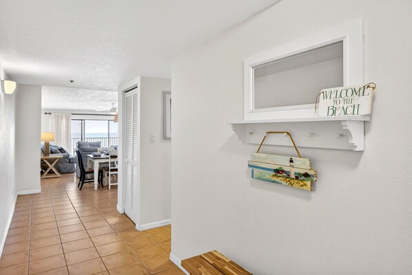 Een gang met uitzicht op het balkon, een welkomstbord en een klein plankje met decoratieve spullen.