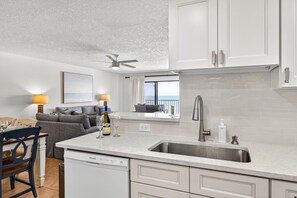 A modern kitchen with white cabinets, a stainless steel sink, and a dining area with a table and chairs. - Beach Palms - Direct Gulf Front Condo (Indian Shores)