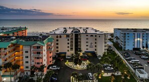A hotel with a central courtyard, multiple balconies, and a view of the ocean at sunset. - Beach Palms - Direct Gulf Front Condo (Indian Shores)
