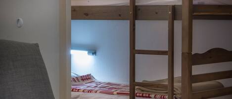 A bunk bed with a wooden frame, a grey sofa, and a red pillow.