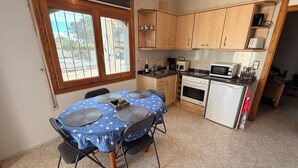 A compact kitchen with wooden cabinets, a microwave, an oven, and a dining table with a blue tablecloth. - Amarella Costa Dorada 1-bedroom apartment with pool (Les Tres Cales)