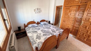 A bedroom with a bed, wooden wardrobe, and a radiator. - Amarella Costa Dorada 1-bedroom apartment with pool (Les Tres Cales)