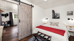 Een slaapkamer met een bed, een rode deken, een houten deur, een bureau en een stoel.