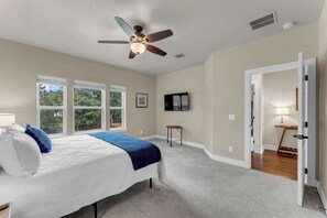 A bedroom with a bed, ceiling fan, windows, TV, and a door leading to another room. - Holiday House - Pool, Boat Lift, & Lake Access (Granite Shoals)