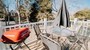 Un terrazzo con una griglia barbecue, un tavolo, sedie e un ombrellone.