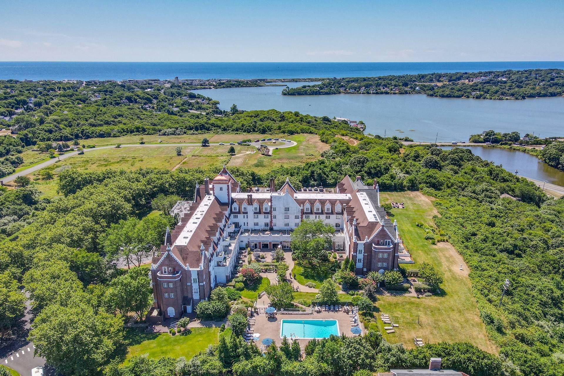 A large, historic building with a central courtyard and a swimming pool, surrounded by lush greenery and a lake.