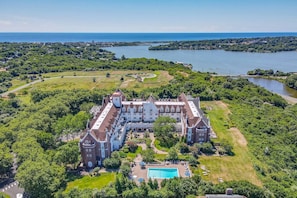A large, historic building with a central courtyard and a swimming pool, surrounded by lush greenery and a lake. - Brand Newly Renovated Resort Style One Bedroom Luxury Suite Simplex (Montauk)