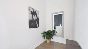 Un pasillo con una planta en maceta, un cuadro enmarcado y un espejo que refleja un baño.