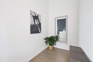 Een gang met een potplant, een lijst met foto en een spiegel die een badkamer weerspiegelt.
