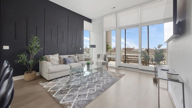 Una sala de estar moderna con sofá, mesa de centro y ventanas amplias que ofrecen vistas a la ciudad.