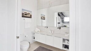 Un baño moderno con inodoro, dos lavabos, un espejo grande y un panel de mármol.