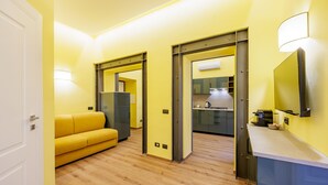 A modern interior with a yellow wall, a wooden floor, a yellow sofa, a kitchen area, and a door. - Satriano Essence of Chiaia Flat (Naples)