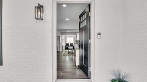 A hallway with white brick walls, a black door, and a potted plant. - 4-bed/2-bath Spacious House in Charming Columbus, Game Day Home, Fenced Backyard (Columbus)