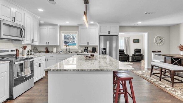 A modern kitchen with white cabinetry, a stainless steel refrigerator, and a marble island. - 4-bed/2-bath Spacious House in Charming Columbus, Game Day Home, Fenced Backyard (Columbus)