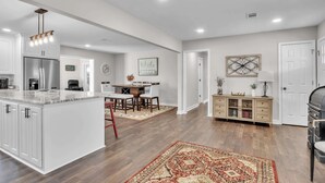 A modern kitchen with a central island, a dining area with a wooden table and chairs, and a living area with a sofa and a lamp. - 4-bed/2-bath Spacious House in Charming Columbus, Game Day Home, Fenced Backyard (Columbus)