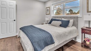 A bedroom with a bed, a ceiling fan, a window with a view, a door, and a nightstand with a lamp. - 4-bed/2-bath Spacious House in Charming Columbus, Game Day Home, Fenced Backyard (Columbus)