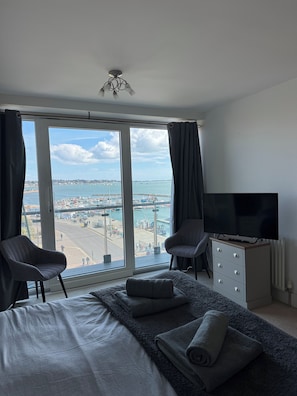 A bedroom with a large window, a bed, two chairs, a TV, and a dresser. - The Lookout-2BR Apartment on Poole Quay Waterfront with Free Parking (Poole)
