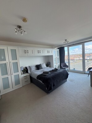 A bedroom with a bed, a wardrobe, a chair, and a large window with a view. - The Lookout-2BR Apartment on Poole Quay Waterfront with Free Parking (Poole)