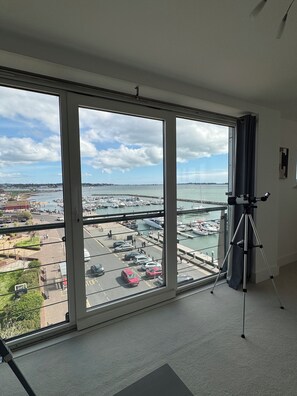 A room with large windows offering a view of a marina with boats and a distant shoreline. - The Lookout-2BR Apartment on Poole Quay Waterfront with Free Parking (Poole)