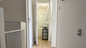 A narrow hallway with wooden flooring, white walls, and a white door leading to a bathroom. - Cosy T3 apartment for 6 people in the heart of Paimpol (Paimpol)