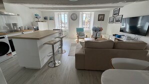 A modern kitchen with a central island, a dining area with a sofa and chairs, a living room with a TV, and a large window with a view. - Cosy T3 apartment for 6 people in the heart of Paimpol (Paimpol)
