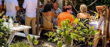 Une réunion en plein air où les participants sont assis à des tables, entourés de verdure et d’un mur de pierre.