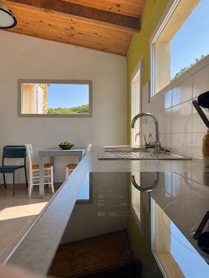 Una cuina moderna amb sostre de fusta, una finestra amb vistes, un rentapeus i una zona de menjador amb cadires i taula.