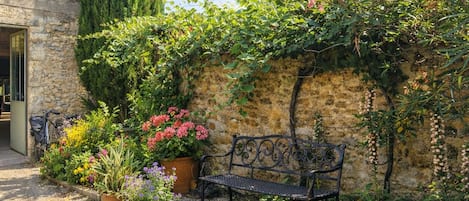 A stone wall with climbing plants, a bench, and potted flowers.