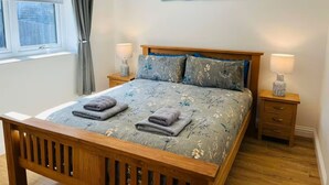 Um quarto com cama de madeira, duas mesas de cabeceira, uma janela com cortinas e um quadro na parede.