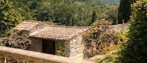 A stone balustrade overlooking a lush garden with a stone building in the background.