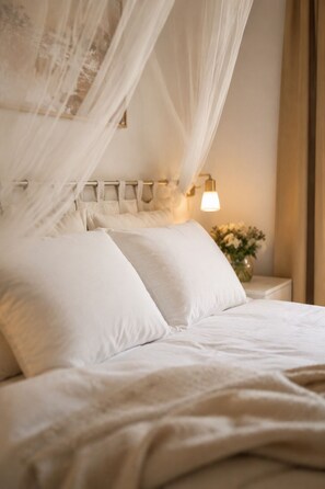 A bed with white bedding and a canopy, a bedside table with a lamp, and a vase with flowers. - Le Mas d'Eylieux - Châteaunette - Haven of peace with swimming pool - South Ardèche (Saint Montan)