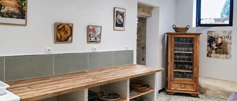 Cozinha com mesa de madeira, prateleiras com utensílios de cozinha, armário com copos e decoração na parede.