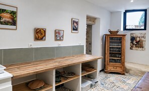 Una cocina con una mesa de madera, repisas con utensilios de cocina, un armario con cristalería y decoración en la pared.