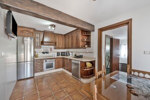 A kitchen with wooden cabinets, a refrigerator, a dishwasher, and a dining table. - Casa el mure: a charming retreat in the heart of the Ronda mountains (Ronda)