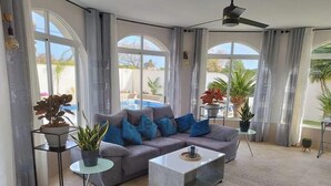 A living room with a grey sofa, blue cushions, a glass coffee table, and potted plants.