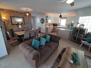 A modern living room with a brown sofa, dining area, kitchen, and a large window.