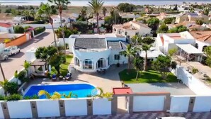 A residential area with a large house featuring a swimming pool, surrounded by palm trees and other houses.