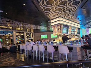 A bar area with a modern design, including a bar counter, seating, and decorative ceiling patterns.
