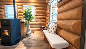 Ein Blockhaushaus-Interieur mit Kaminofen, einer Bank mit Kissen, einer Topfpflanze und Holzwänden.