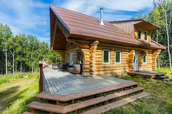 A log cabin with a deck, a chimney, and a porch with outdoor furniture.