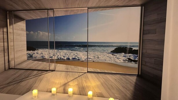 Ein Zimmer mit einem großen Spiegel, der eine Strandkulisse reflektiert, einem weißen Schrank mit Kerzen und Holzboden.