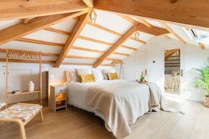 A bedroom with a sloped ceiling, a bed with a beige blanket, a bedside table, a chair, and a potted plant. - Villa De Los Leones - Seven Bedroom Villa, Sleeps 19 (Sitges)