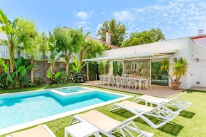 Ein Pool mit Liegestühlen, eine überdachte Terrasse mit Esstisch und üppiges Grün.