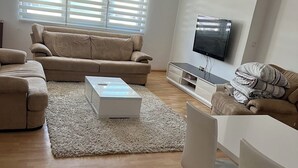 Una sala de estar moderna con un sofá color beige, una mesa de centro blanca y un televisor de pantalla plana montado en la pared.